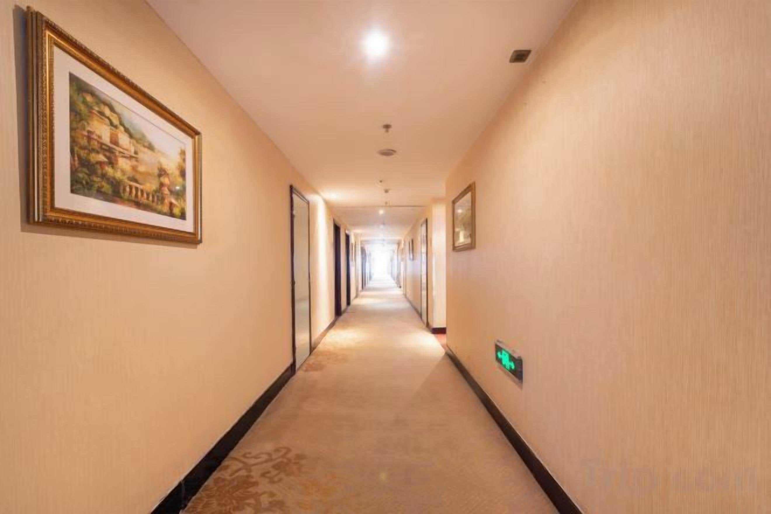 A hotel hallway with framed artwork on the walls, a carpeted floor, and a green exit sign.
