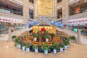 A hotel lobby with a central floral arrangement, a large wall art piece, and a staircase with glass railings.