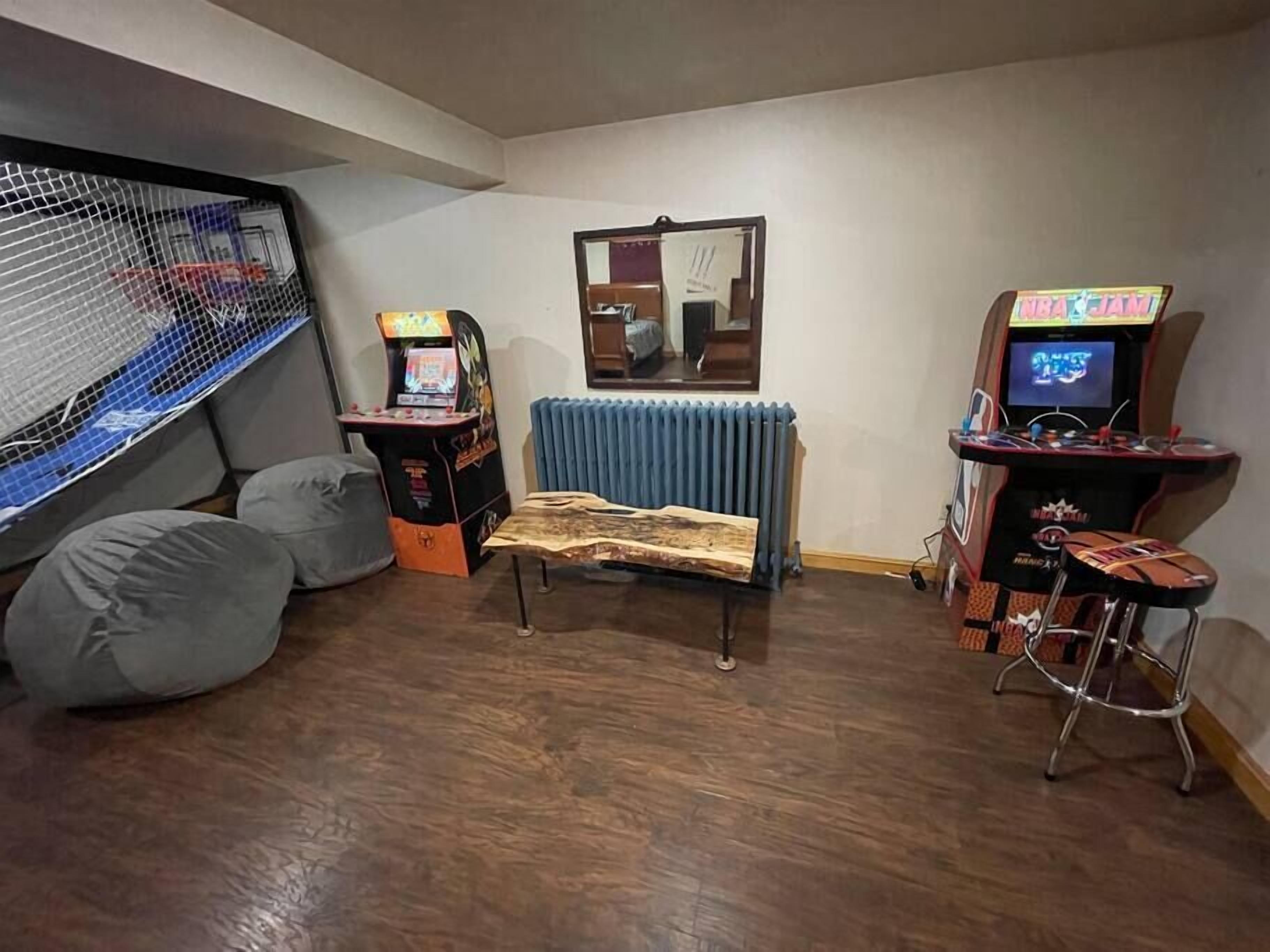 Een kamer met een houten vloer, een kleine bankje, twee loungestoelen en twee speelautomaten.