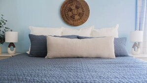 A bed with a textured blue quilt, a round woven wall hanging, and a bedside lamp. - Pet friendly | 5 min walk to sand | full kitchen (Myrtle Beach)
