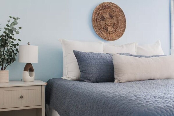 A bed with a blue quilt, white pillows, and a round woven wall hanging.