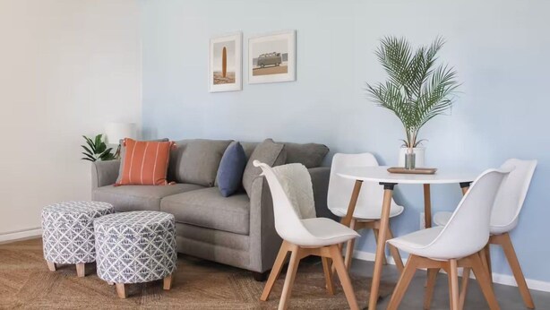 A living room with a grey sofa, patterned ottomans, a white table with chairs, and a potted plant. - Pet friendly | 5 min walk to sand | full kitchen (Myrtle Beach)