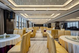 Un comedor amplio con mesas y sillas redondas, un techo alto con iluminación empotrada y ventanas grandes a un lado.