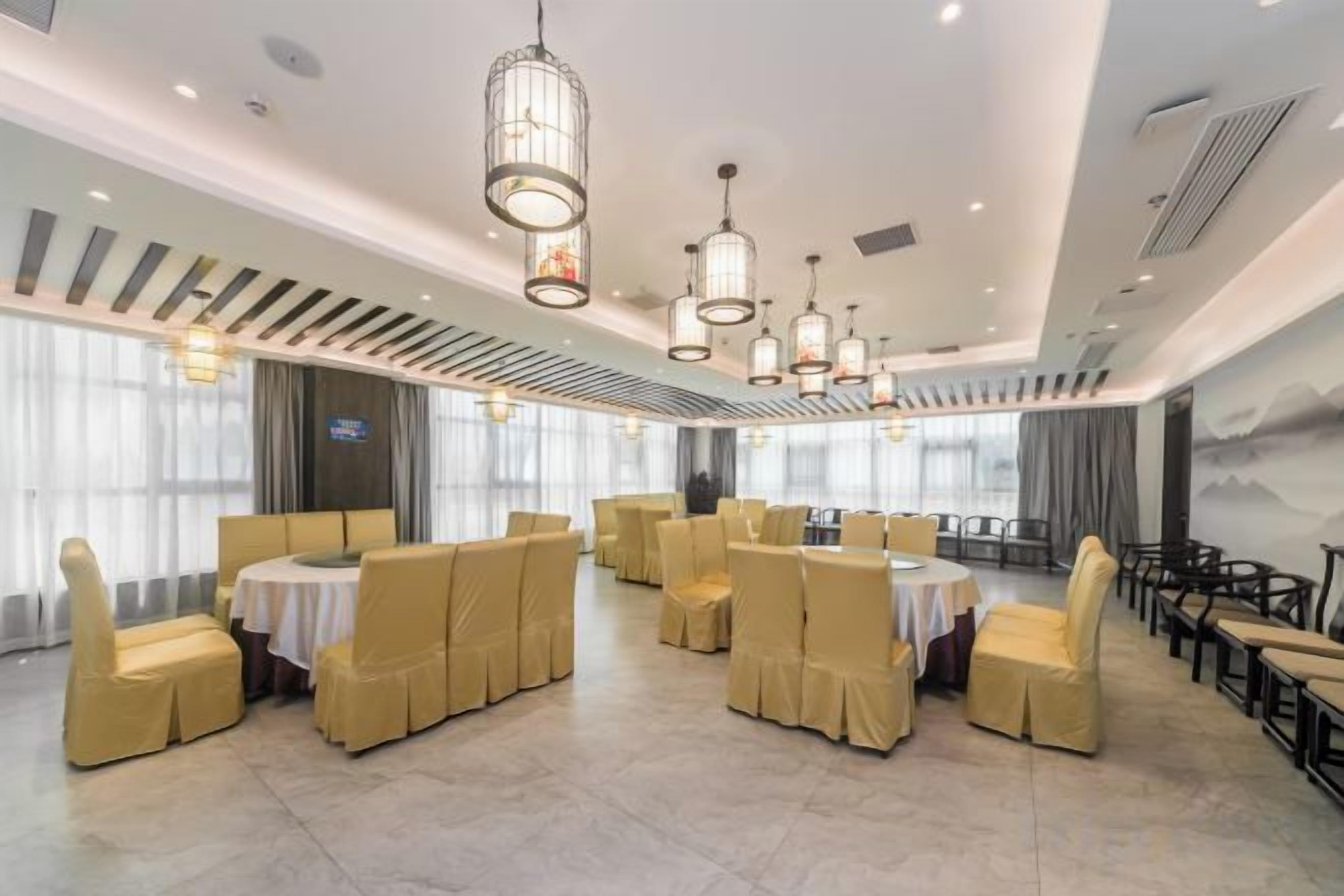 Un salón de banquetes con mesas y sillas redondas, un techo alto con luces colgantes y ventanas amplias.