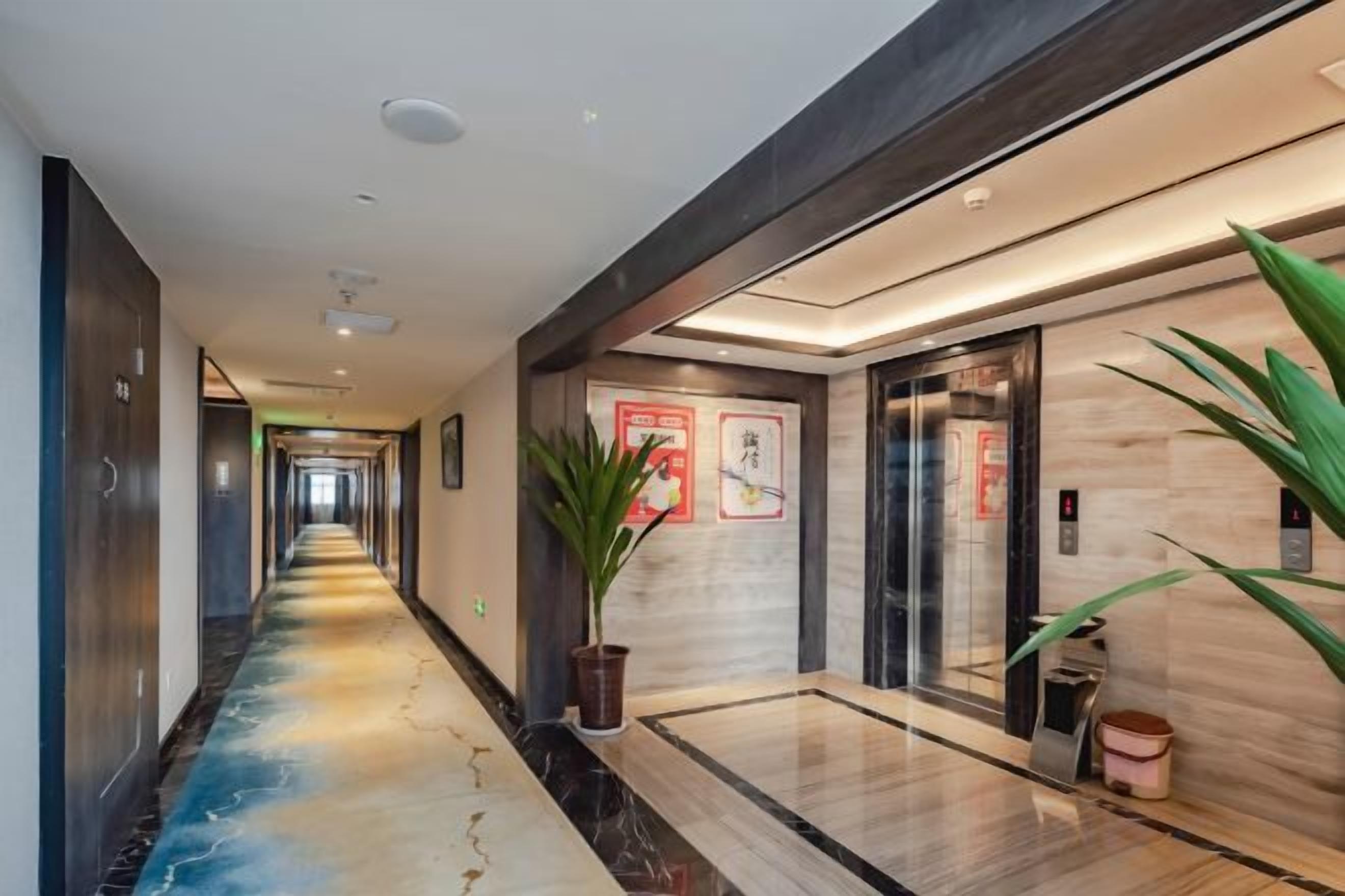 A hotel corridor with a long, narrow hallway, a reception desk, and a reception area with a plant.