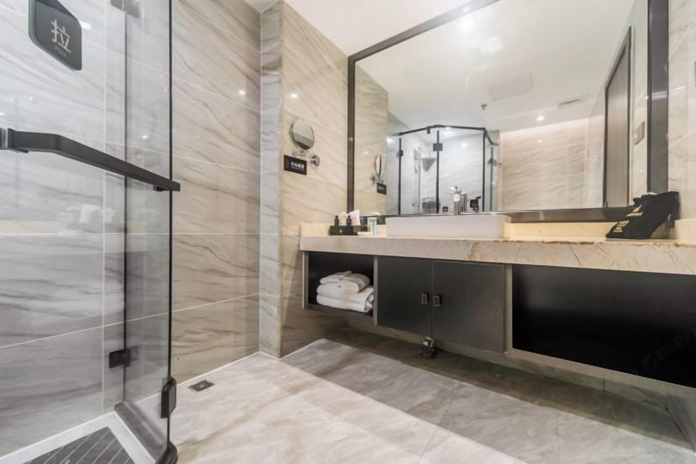 A modern bathroom with a glass shower enclosure, a large mirror, and a marble-tiled floor.