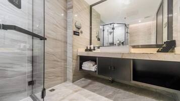 A modern bathroom with a glass shower enclosure, a large mirror, and a marble-tiled floor.