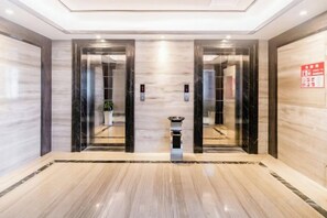 A modern elevator area with marble flooring and glass doors.