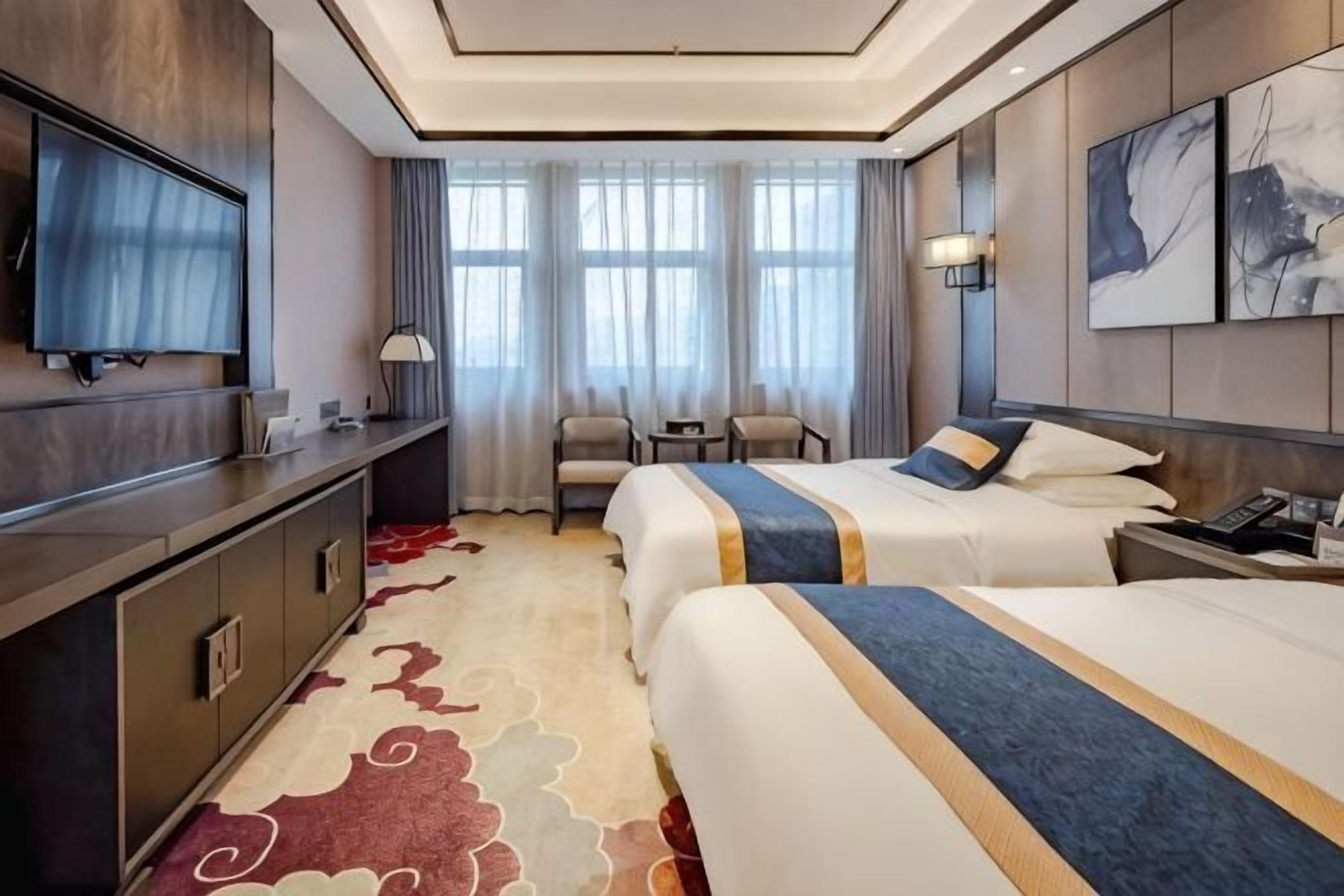 A hotel room with two beds, a desk, a TV, and a view of the city.