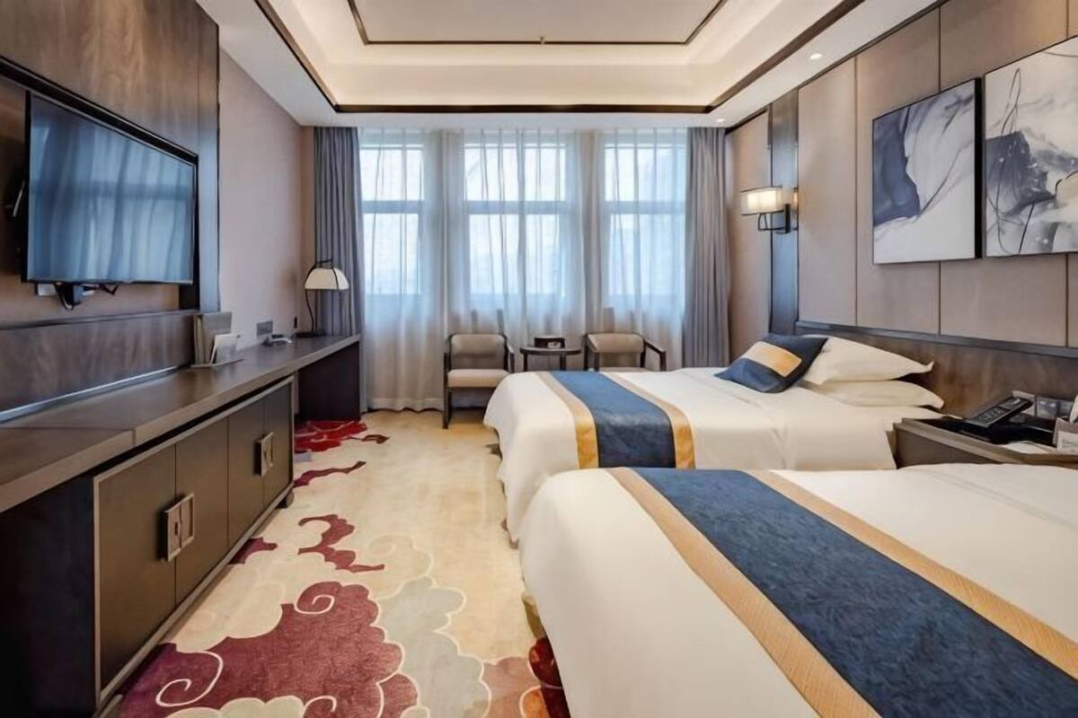 A hotel room with two beds, a desk, a TV, and a view of the city.