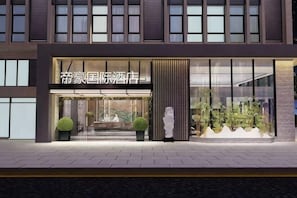 Entrada de hotel con fachada moderna, amplias ventanas y un área de recepción con una estatua.