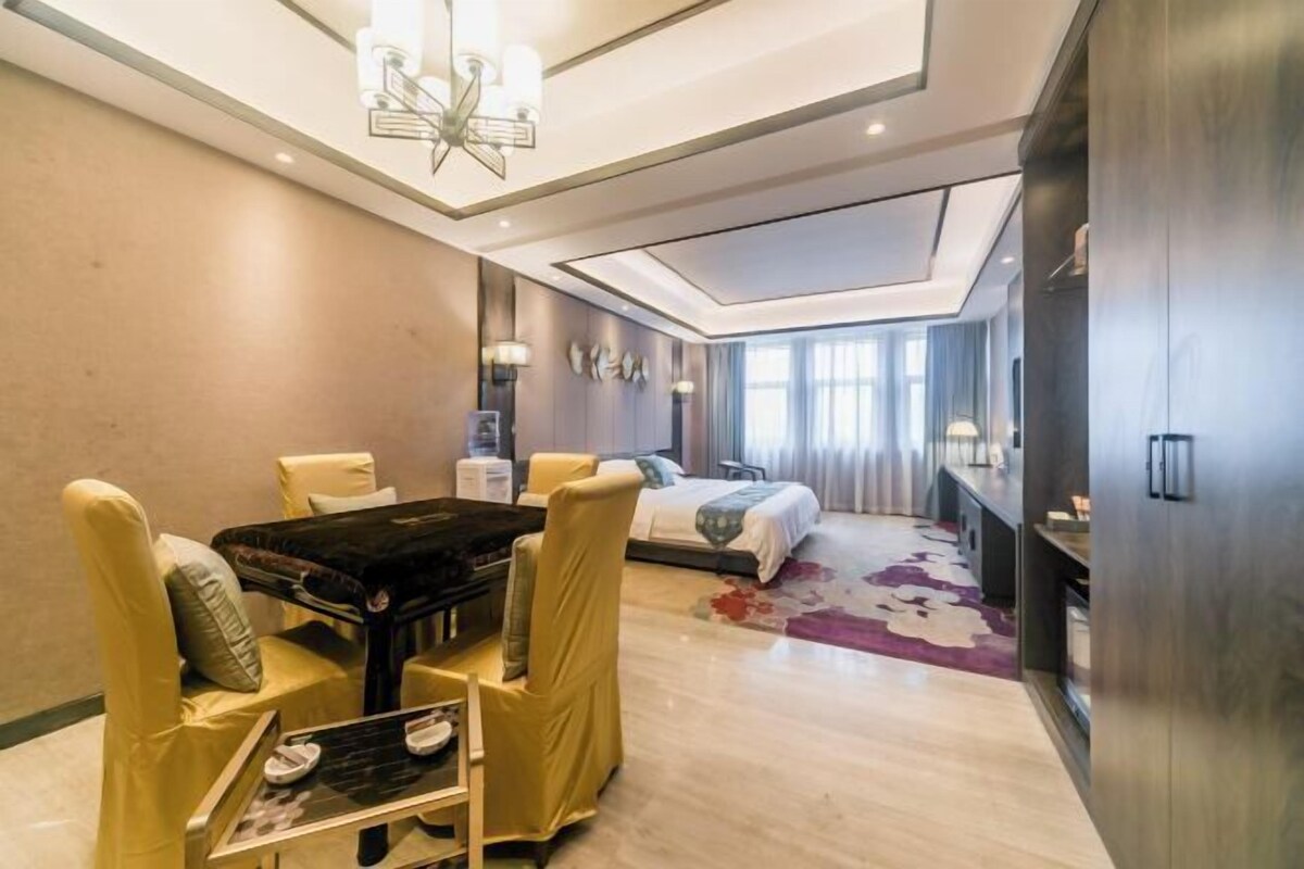 A hotel room with a bed, a desk, a chair, a table, and a TV.