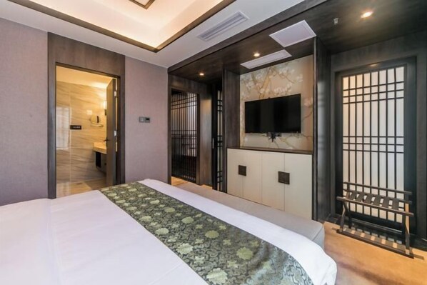 A hotel room with a bed, a TV mounted on the wall, a sliding door, and a small seating area. - Dihao International Hotel (Guang'an)