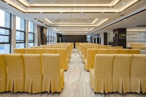 A hotel conference room with rows of yellow chairs, large windows, and a modern ceiling design.