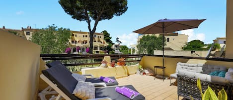 A balcony with lounge chairs, a table, and an umbrella.