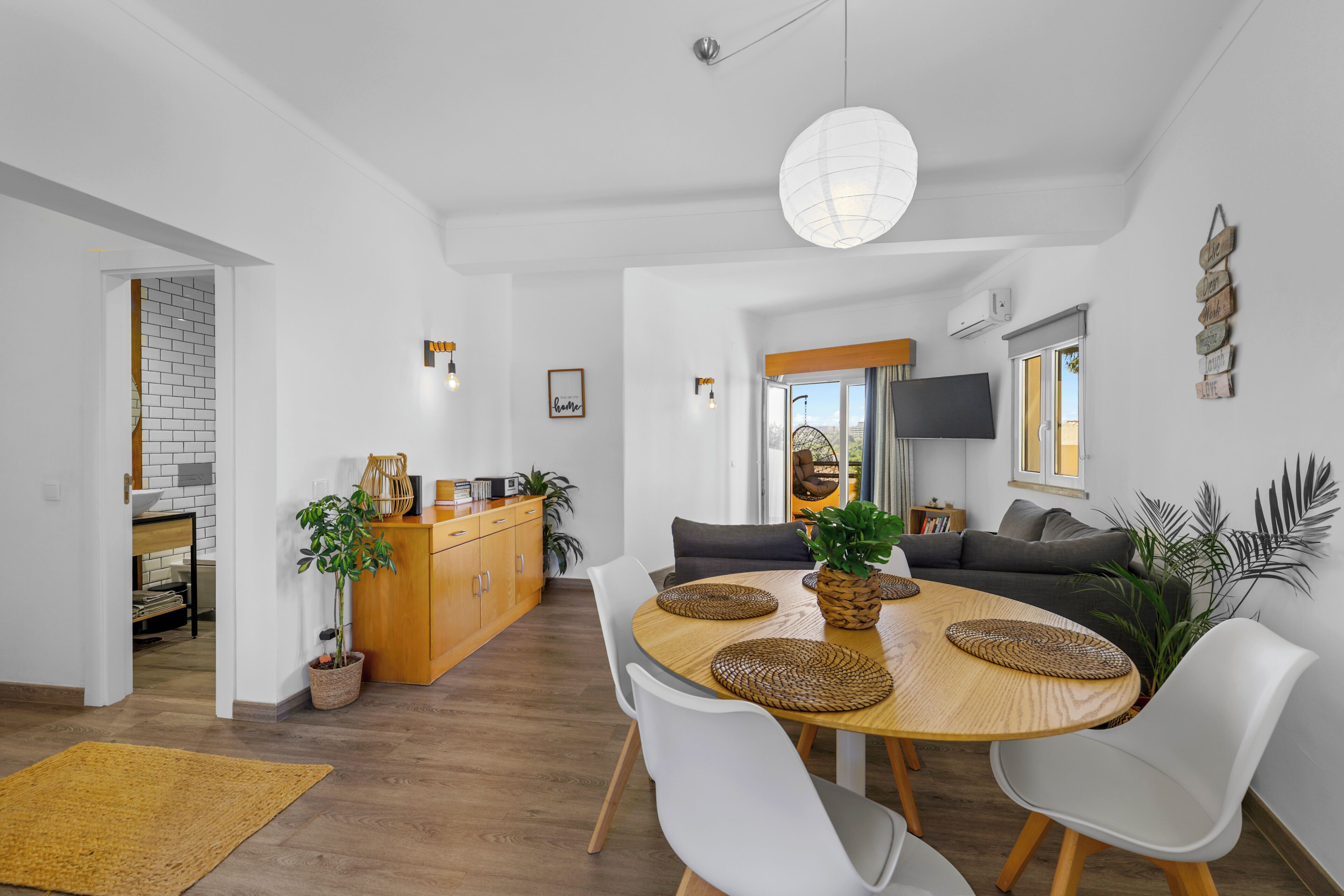 Un soggiorno moderno con un tavolo da pranzo in legno, sedie bianche e un divano. C'è un'area cucina con uno schienale in mattoni e mobili in legno.