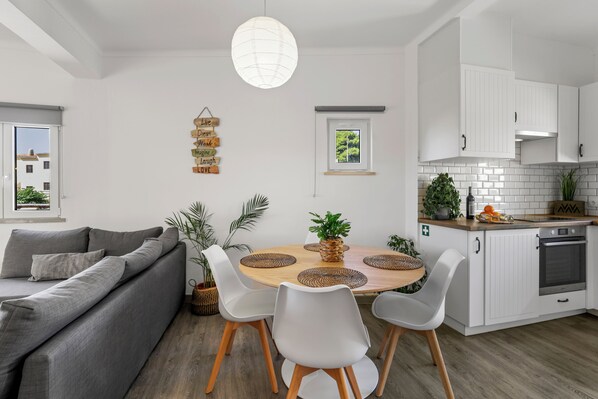 Una cocina moderna con armarios blancos, una mesa de comedor con individuales tejidos y un sofá gris.