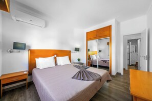 A hotel room with a bed, bedside table, nightstand, and a mirror.