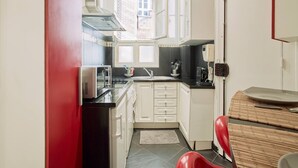 Une cuisine de taille réduite avec des meubles blancs, un plan de travail noir et une chaise rouge.