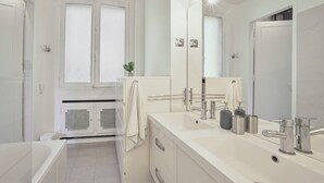 Une salle de bain moderne avec un grand miroir, deux lavabos et une baignoire.