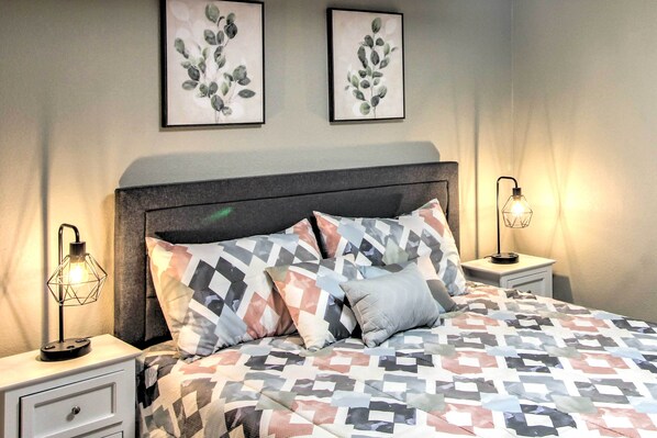 A neatly made bed with patterned bedding, two wall-mounted artworks, and bedside lamps on nightstands.