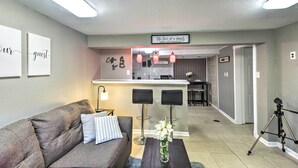 Un salon moderne avec un canapé gris, une décoration murale sur le thème du café, un coin bar avec des tabourets et un trépied dans un coin.