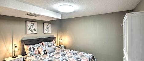 Un dormitorio con cama, mesitas de noche, armario y dos cuadros colgados en la pared.