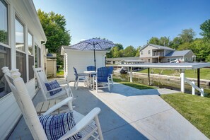 A patio with white chairs and a blue umbrella, a small table, and a view of a house and a body of water. - Waterfront Lakeview Cottage w/ Dock & Lift! (Lakeview)