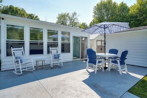 A patio with a table and chairs, a rocking chair, and a patterned umbrella. - Waterfront Lakeview Cottage w/ Dock & Lift! (Lakeview)
