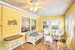 A room with a yellow wall, a white ceiling fan, a striped sofa, and white wicker chairs. - Green Lake Vacation Home w/ Screened Porch! (Markesan)