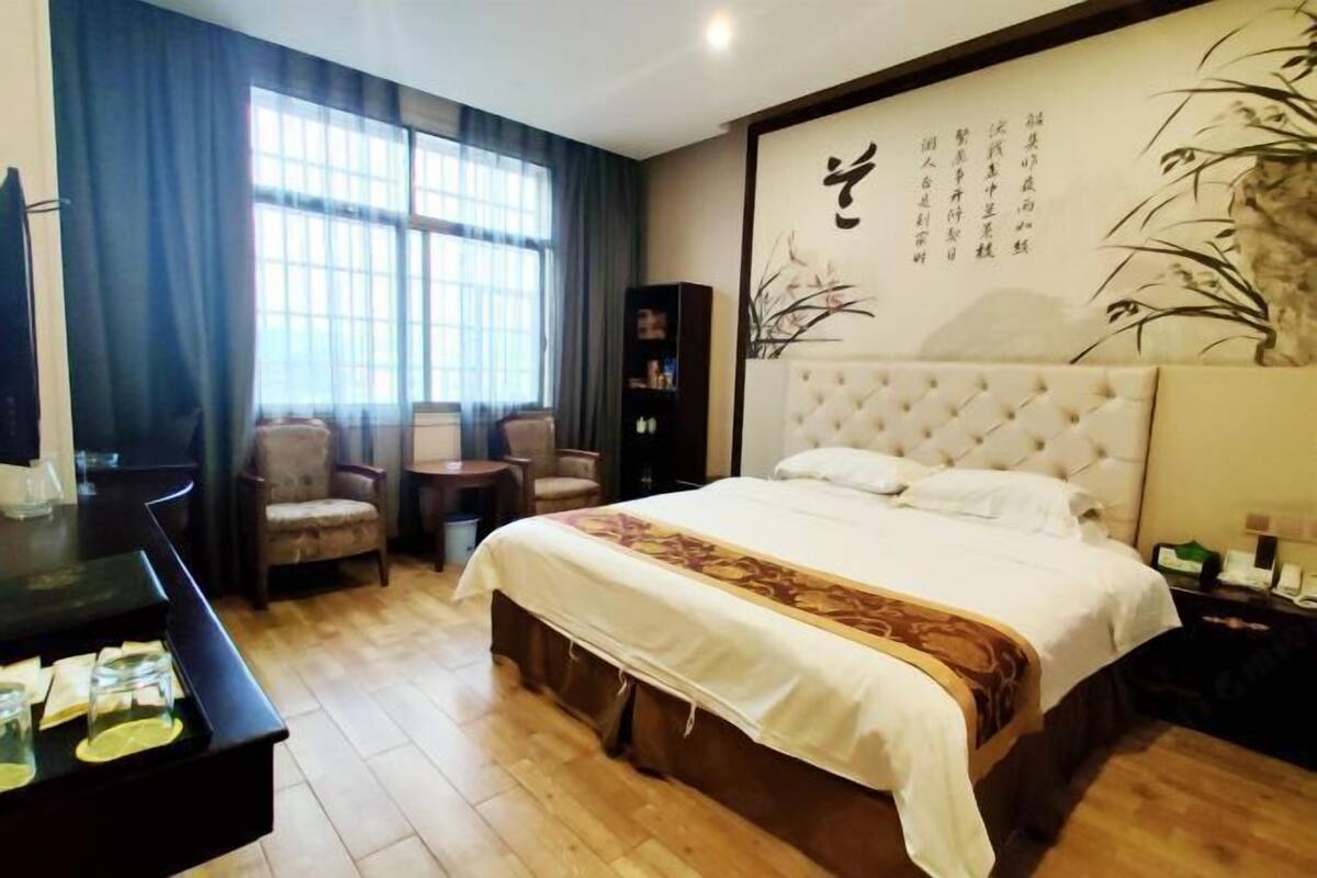 Une chambre d’hôtel avec un grand lit, un bureau avec une chaise, une bibliothèque et une grande fenêtre avec des rideaux.