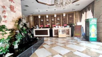 A hotel reception area with a check-in counter, a reception desk, a chandelier, and a green vending machine.