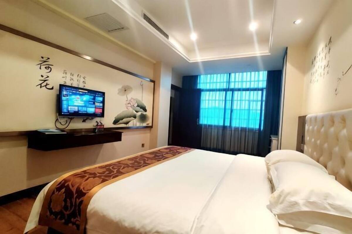 Une chambre d’hôtel avec un grand lit, un téléviseur fixé au mur, une étagère murale et une fenêtre avec des rideaux.