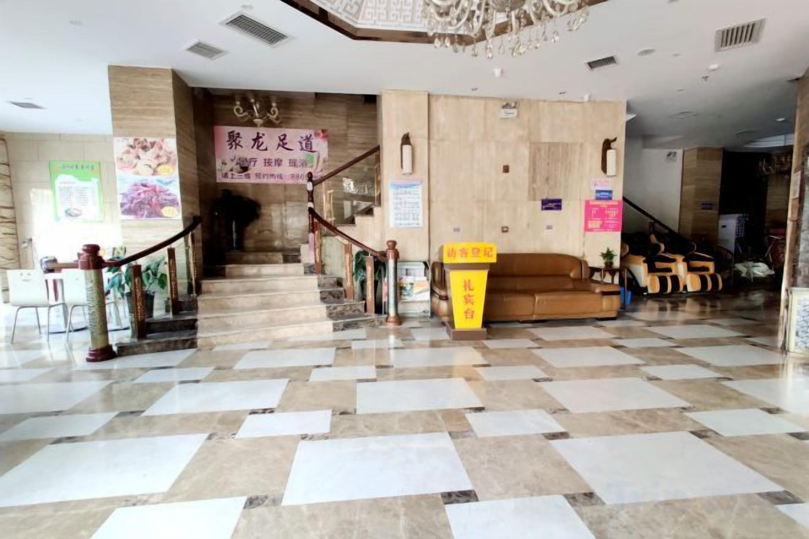 A hotel lobby with a checkered floor, a staircase, a reception desk, and a sofa area.