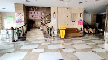 A hotel lobby with a checkered floor, a staircase, a reception desk, and a sofa area.