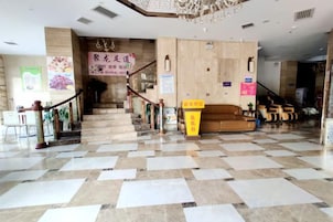 Un vestíbulo de hotel con piso a cuadros, una escalera, un mostrador de recepción y una zona de sofás.