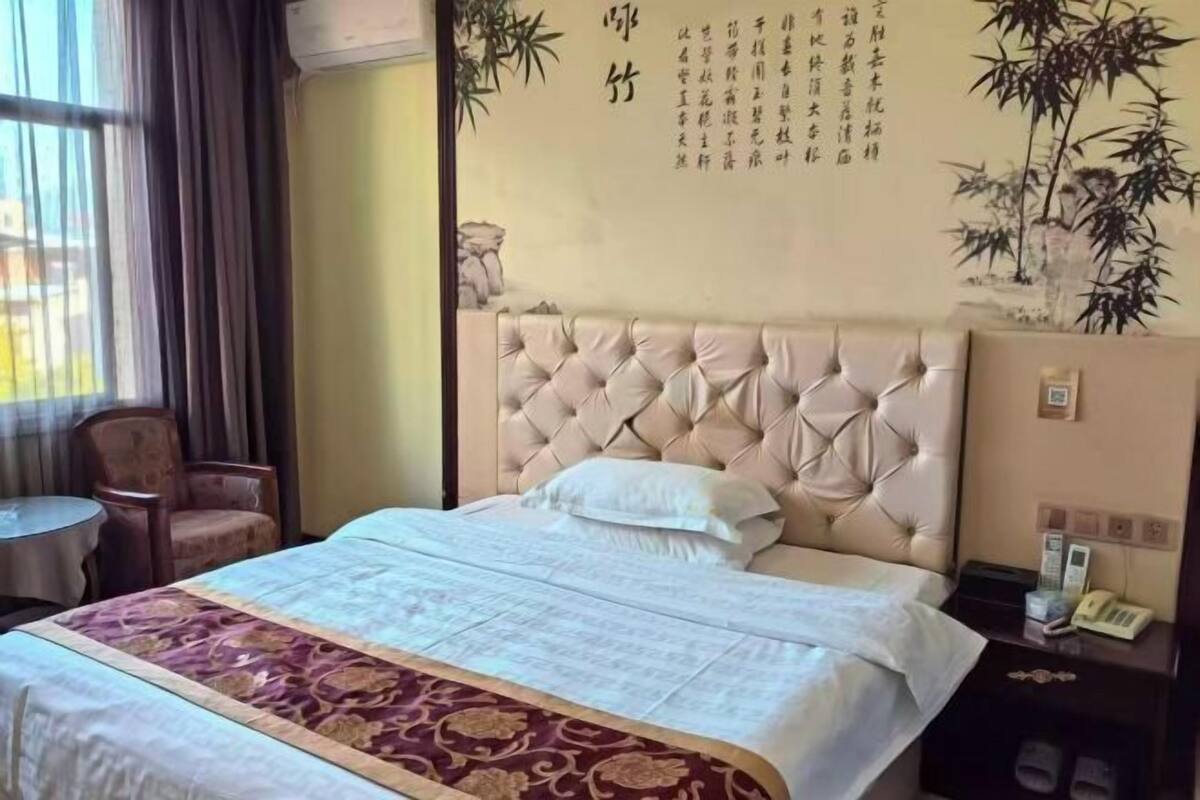 Une chambre d’hôtel avec un grand lit, une table de chevet avec un téléphone et une chaise près de la fenêtre.