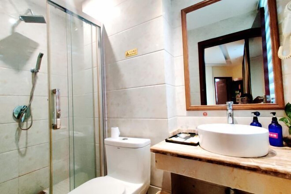 Ein Badezimmer mit Duschkabine aus Glas, Toilette, Waschbecken mit Spiegel darüber und Toilettenartikeln auf der Ablagefläche.