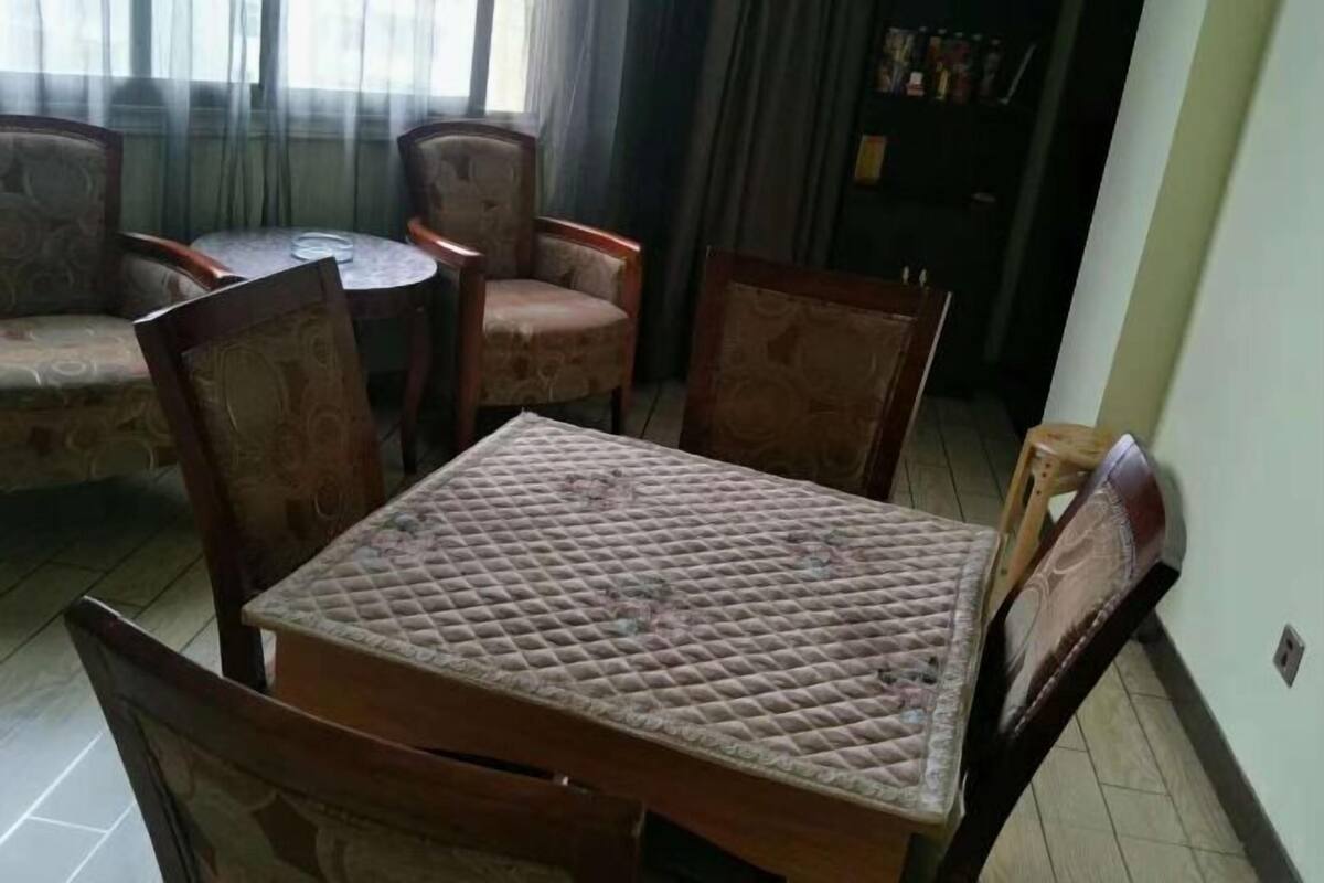 Un coin repas avec une table et quatre chaises, un canapé et une bibliothèque en arrière-plan.