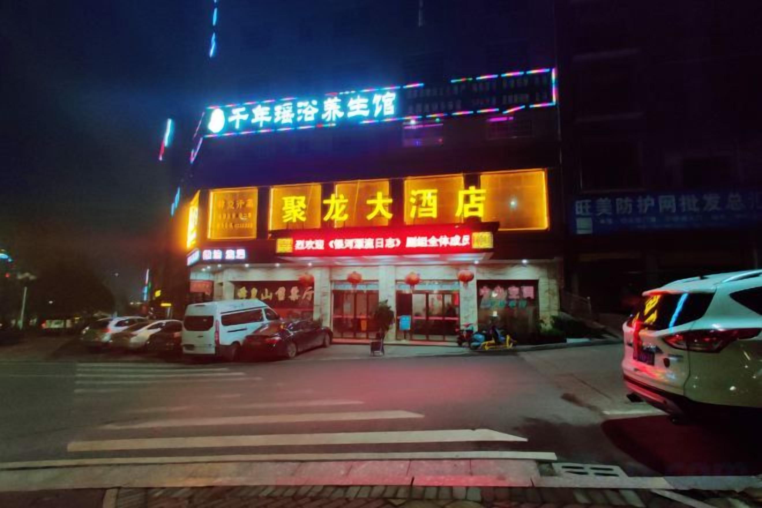 A building with illuminated signage, a crosswalk, and parked cars.