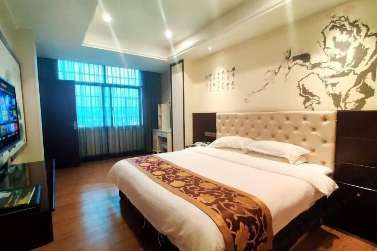 Une chambre d’hôtel avec un grand lit, une télévision, un bureau et une fenêtre avec des rideaux.