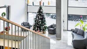 A modern interior with a staircase, a Christmas tree, grey sofas, and large windows. - KORA APARTMENTS (Prague)