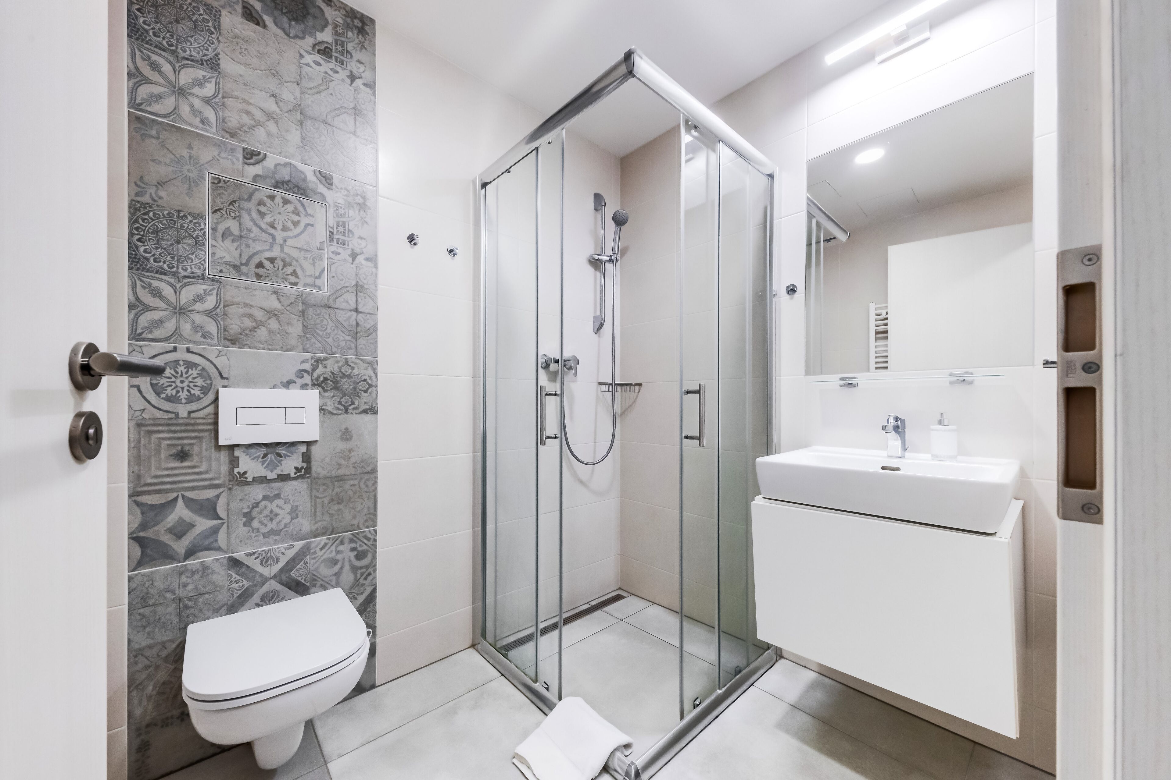 A modern bathroom with a glass-enclosed shower, a white toilet, and a sink with a mirror above it.