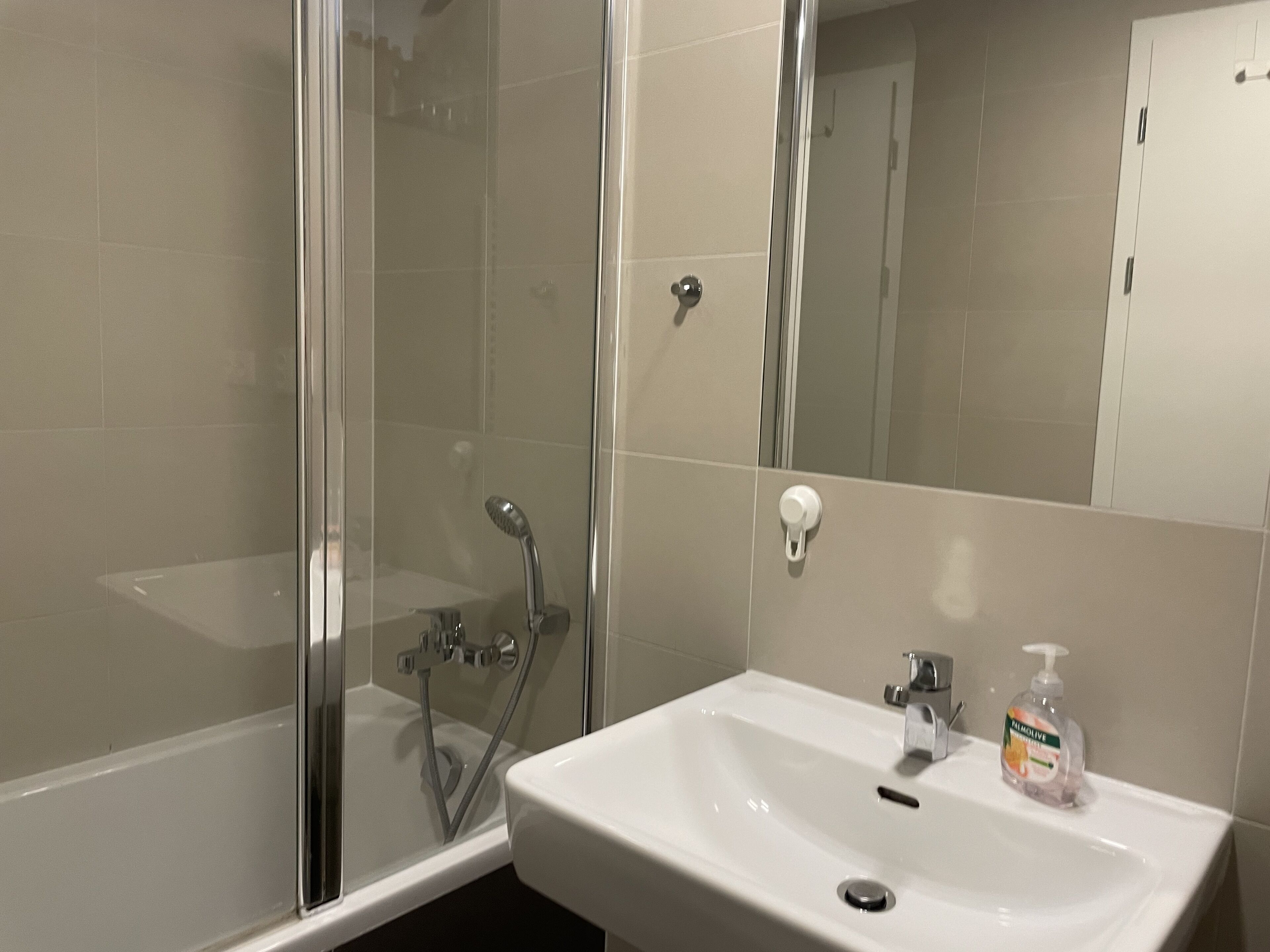 Un baño con cabina de ducha de vidrio, un lavabo blanco y un espejo.
