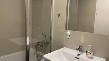 Un baño con cabina de ducha de vidrio, un lavabo blanco y un espejo.
