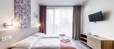 A modern hotel room with a bed, bedside table, TV, and a large window with curtains.