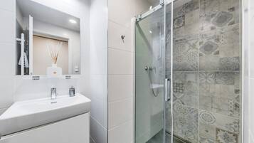 Une salle de bain moderne avec un lavabo blanc, un miroir et une douche en verre, le tout agrémenté de carreaux à motifs.