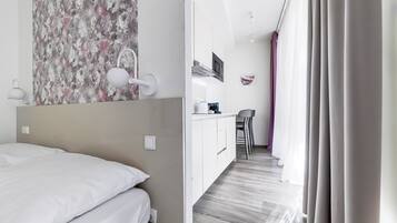 A hotel room with a bed, a small kitchenette, and a view of the hallway.