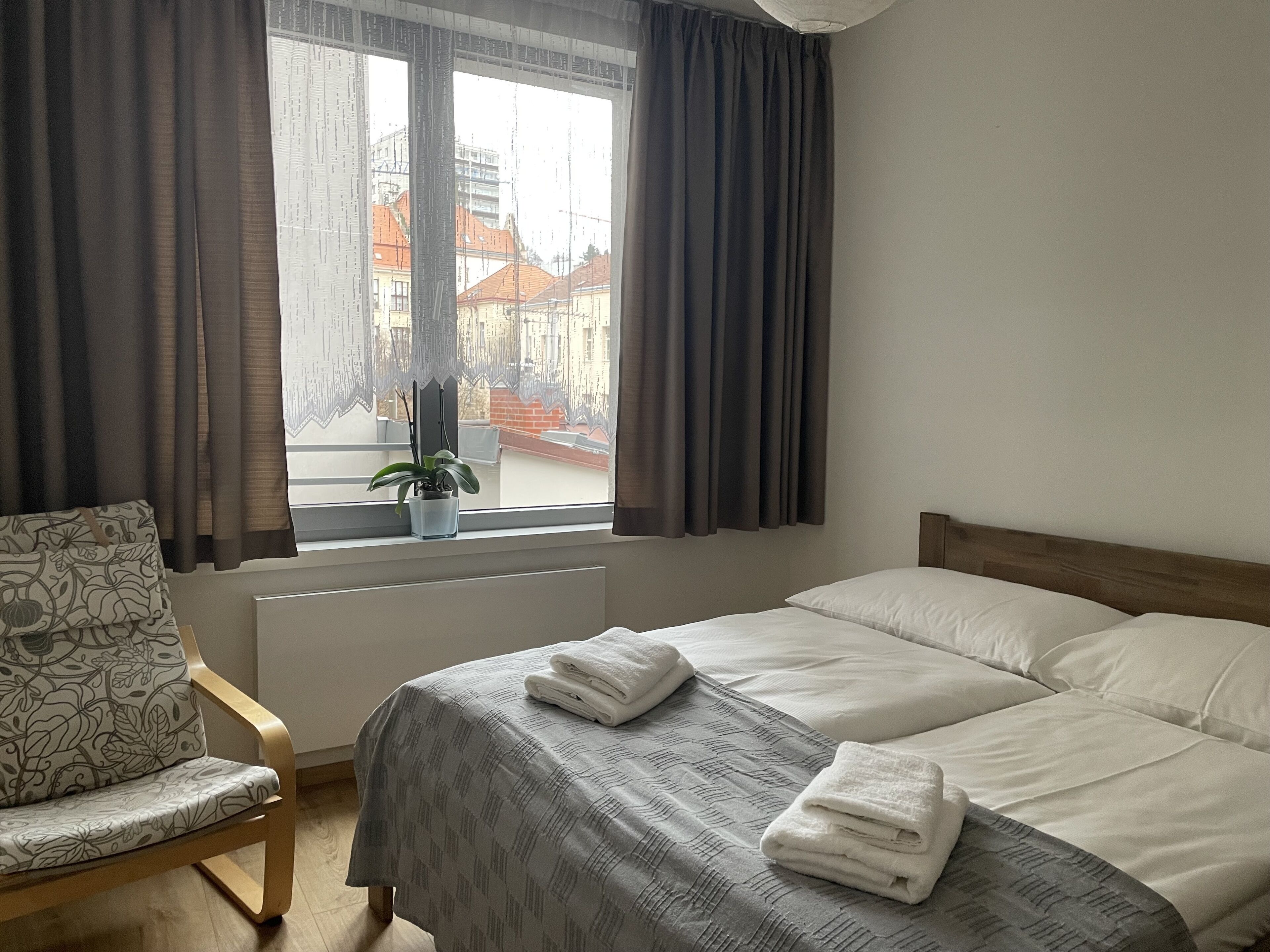 Een hotelkamer met een bed, een stoel, een raam met gordijnen en een potplant op de vensterbank.