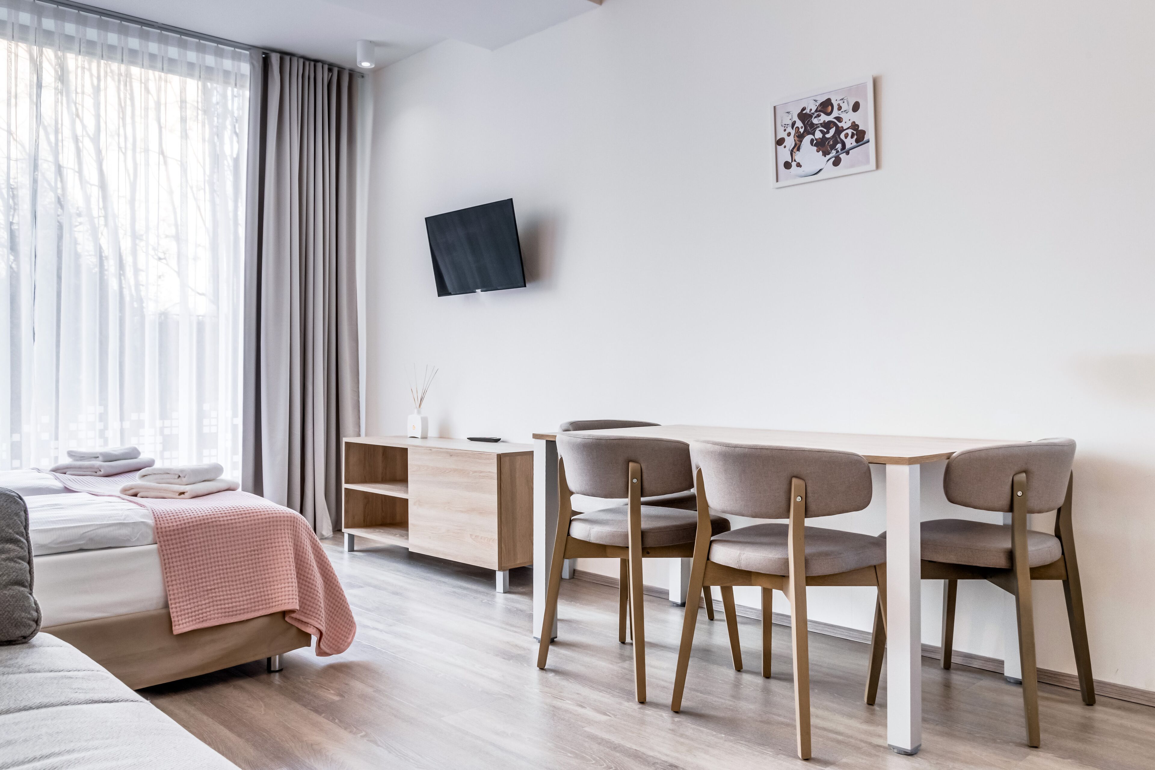 A modern hotel room with a bed, bedside table, and a desk with chairs.